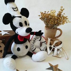 May include: Knitted black and white Mickey Mouse doll wearing a sailor hat and holding a life preserver that says "Steamboat Willie".