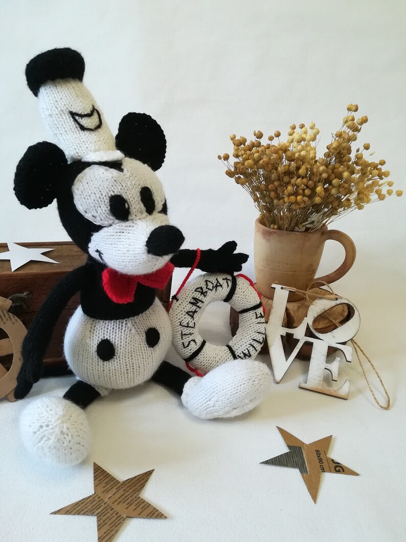 May include: Knitted black and white Mickey Mouse doll wearing a sailor hat and holding a life preserver that says "Steamboat Willie".