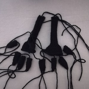 May include: A set of black knitted fingerless gloves with long strings attached. The gloves are laid out on a white surface.
