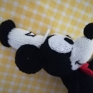 May include: A black and white knitted toy mouse with red bow tie. The mouse is lying on its side with its head tilted back.
