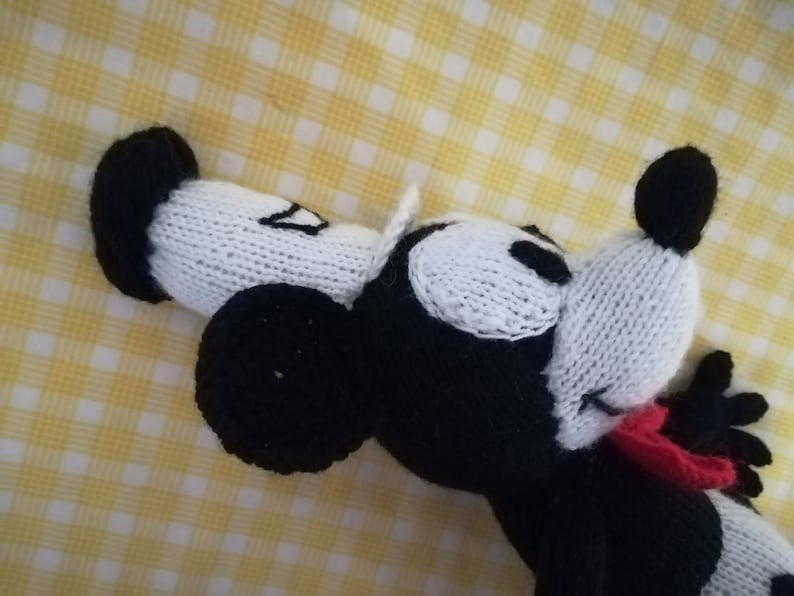 May include: A black and white knitted toy mouse with red bow tie. The mouse is lying on its side with its head tilted back.