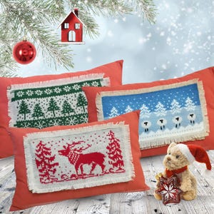 May include: Three decorative throw pillows with a Christmas theme. The pillows are red with a white knit design. One pillow features a reindeer, one features a winter scene with trees and snow, and one features a winter scene with trees and sheep.