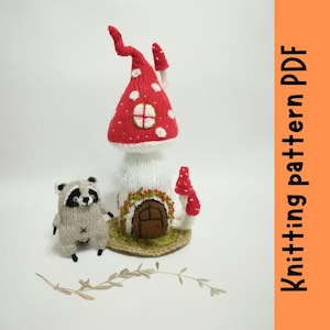 Könnte beinhalten: Strickmuster PDF für ein Pilzhaus mit einem rot-weißen Dach, einem weißen Körper und einer braunen Tür. Ein kleiner grauer Waschbär steht vor dem Haus.