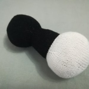 May include: A black and white knitted dumbbell toy. The dumbbell is made of two round balls connected by a cylindrical piece.