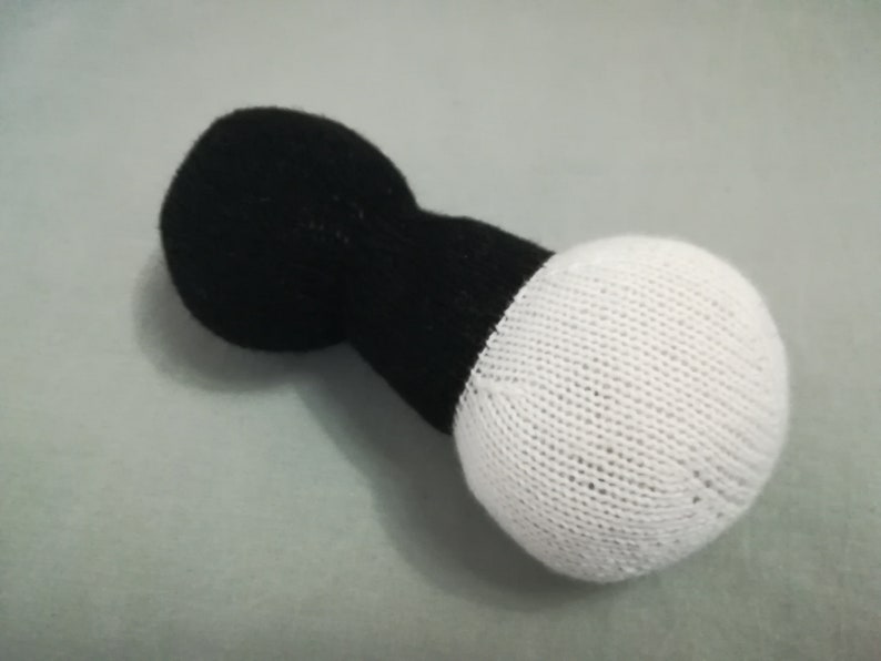 May include: A black and white knitted dumbbell toy. The dumbbell is made of two round balls connected by a cylindrical piece.