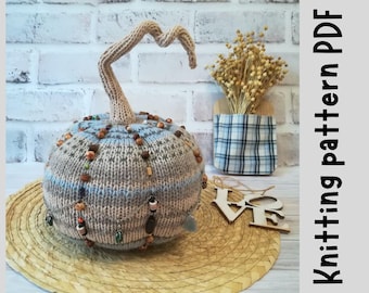 Può includere: Zucca di lana con un gambo marrone e un motivo blu e grigio. La zucca è decorata con perline e una catena. La zucca è appoggiata su un tappetino di paglia intrecciato.