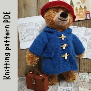 May include: A knitted blue coat with a hood and brown wooden toggles. The coat is worn by a brown teddy bear with a red hat. The bear is holding a brown suitcase. The image includes the text "Knitting pattern PDF".