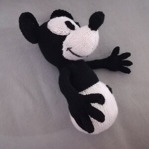 May include: Black and white knitted plush toy resembling a cartoon mouse. The toy has a large, round head with a white face and black eyes. The body is black with white accents.
