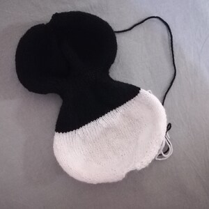 May include: A black and white knitted hat with a long string attached. The hat is partially turned inside out, revealing the white knit lining.