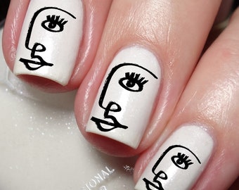 May include: Three fingernails painted with a glossy white base coat, each featuring a black line art illustration of a stylized human face profile. The design includes a single eye with lashes, a nose, and lips, creating a continuous line drawing.