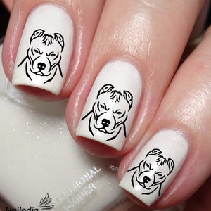 Puede incluir: Tres uñas blancas con diseños de arte de línea negra de la cabeza de un perro pitbull. El esmalte de uñas es de un blanco brillante.