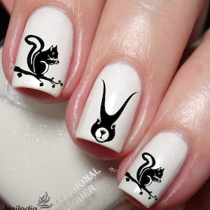 May include: Close-up of three white fingernails with black nail art. The nail art features a squirrel design on two nails and a rabbit design on one nail.