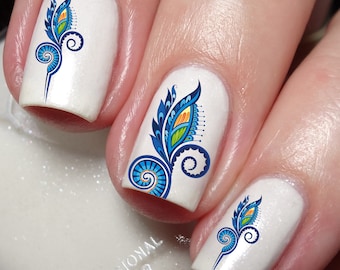 May include: Three fingernails painted with a glossy white base coat, each featuring a detailed nail art decal. The design consists of a stylized blue, green, and orange feather-like motif with intricate swirling lines and fine, delicate details.