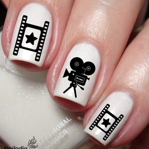 May include: Close-up of fingernails with black and white nail art featuring film reels and a vintage movie camera. The nails are painted white.