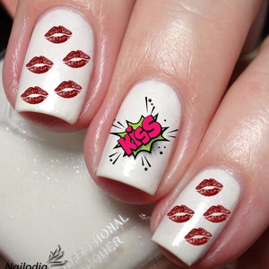 May include: White nail polish with red lip decals and a comic-style "KISS" graphic. The nails are professionally done, showcasing a fun and flirty design. The nail art is a playful accessory.