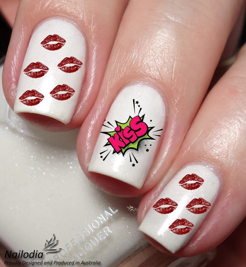 May include: White nail polish with red lip decals and a comic-style "KISS" graphic. The nails are professionally done, showcasing a fun and flirty design. The nail art is a playful accessory.