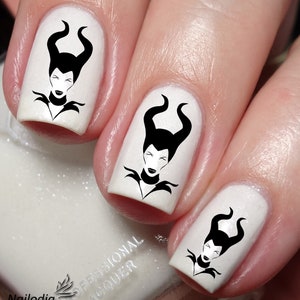 May include: Close-up of three white fingernails with black nail art decals of Maleficent from Disney's Sleeping Beauty. The decals feature Maleficent's face with horns and a pointed collar.