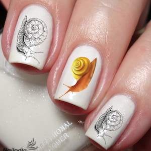 Könnte beinhalten: Nahaufnahme von drei Fingernägeln mit Schnecken-Nageldesign-Aufklebern. Ein Nagel hat eine schwarz-weiße Schnecke, ein anderer eine gelbe und braune Schnecke und der dritte Nagel eine schwarz-weiße Schnecke.