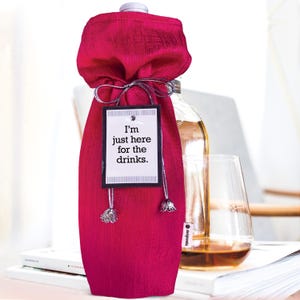 May include: A pink wine bottle bag with a silver ribbon and a tag that says "I'm just here for the drinks."