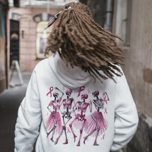 Pu&ograve; includere: Felpa con cappuccio bianca con un disegno di scheletri danzanti in tut&ugrave; rosa e nastri rosa. Il design include nastri rosa per la sensibilizzazione al cancro al seno. La felpa ha un cappuccio con coulisse e maniche lunghe.