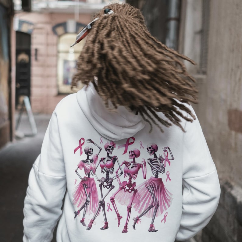 Pu&ograve; includere: Felpa con cappuccio bianca con un disegno di scheletri danzanti in tut&ugrave; rosa e nastri rosa. Il design include nastri rosa per la sensibilizzazione al cancro al seno. La felpa ha un cappuccio con coulisse e maniche lunghe.