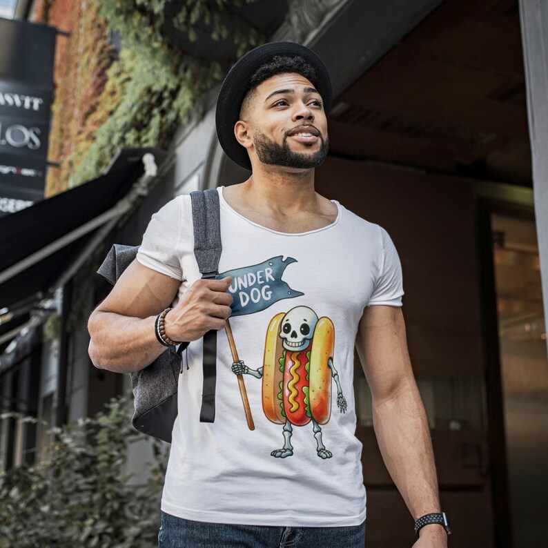 May include: A white t-shirt featuring a graphic of a skeleton hot dog holding a flag that reads "Under Dog".