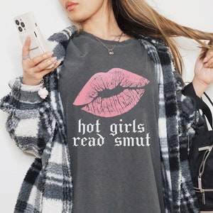 Model is wearing comfort colors oversized tee in pepper with hot girls read smut in white and lipstick print in pink