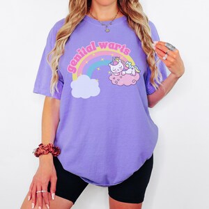 model is wearing comfort colors tee in violet with genital warts design on front with a rainbow stars and a unicorn
