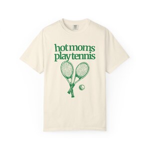 model is wearing comfort colors short sleeve shirt in ivory with hot moms play tennis graphic in green on front