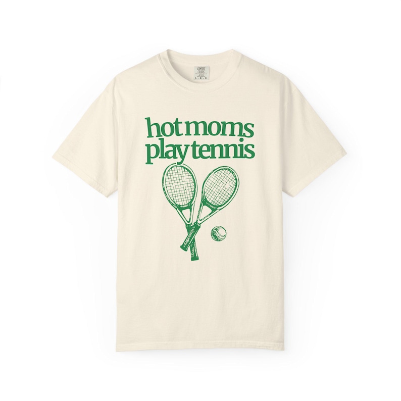 model is wearing comfort colors short sleeve shirt in ivory with hot moms play tennis graphic in green on front