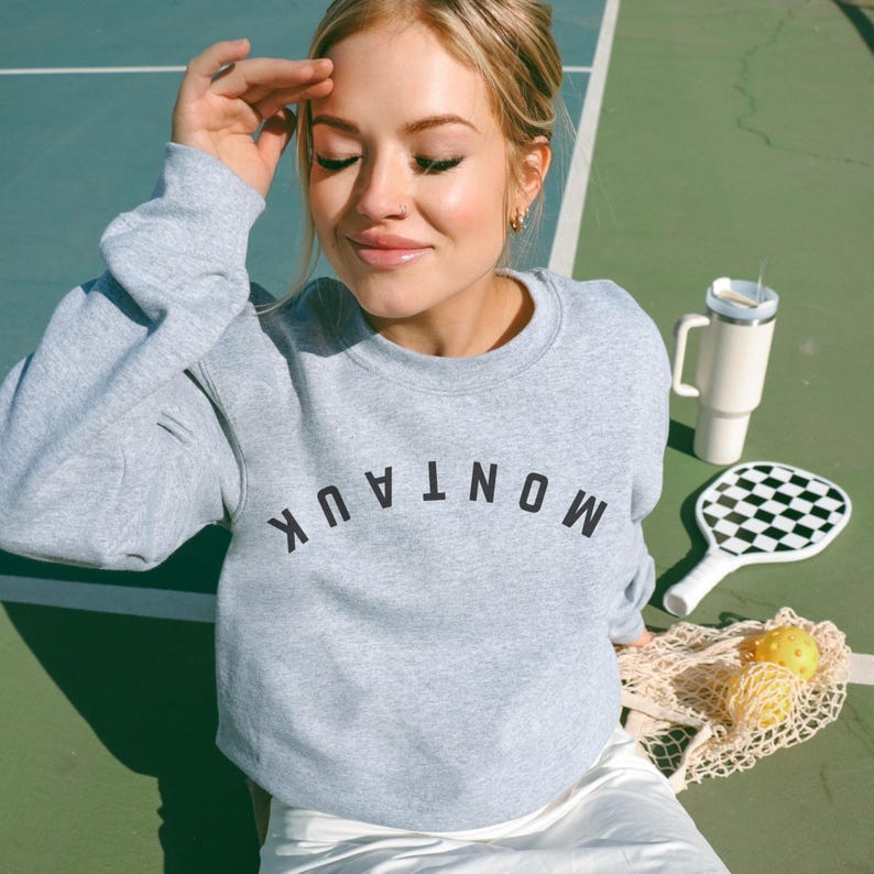 model is wearing gildan oversized crewneck sweatshirt in sport gray with upside down montauk in black across front