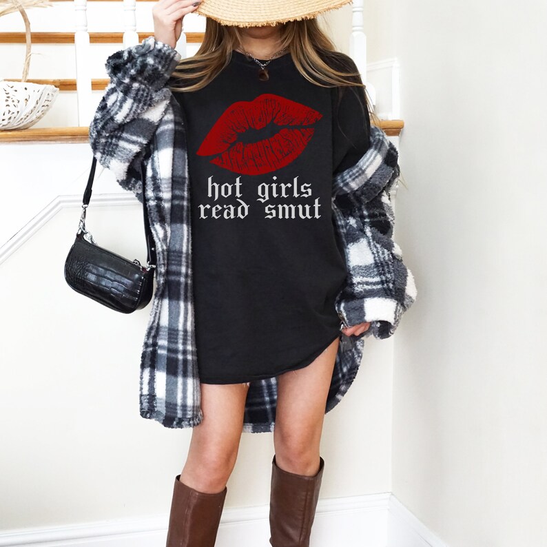 Model is wearing comfort colors oversized tee in black with hot girls read smut in white and lipstick print in red
