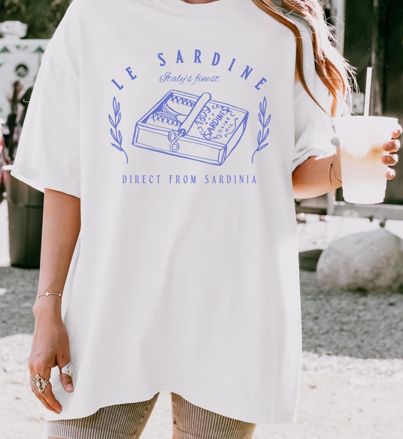 model is wearing comfort colors oversized tee in white with le sardine can and italy's finest direct from sardinia in blue on front