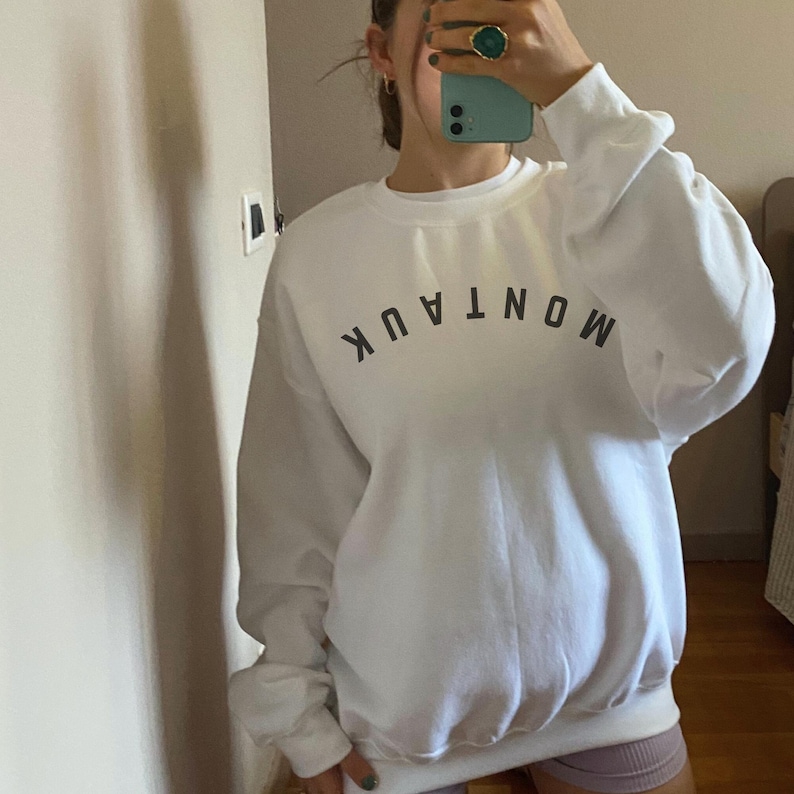 model is wearing gildan oversized crewneck sweatshirt in white with upside down montauk in black across front