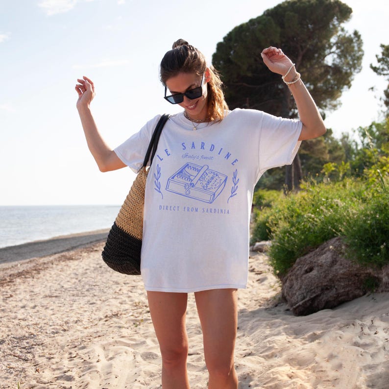 model is wearing comfort colors oversized tee in white with le sardine can and italy's finest direct from sardinia in blue on front