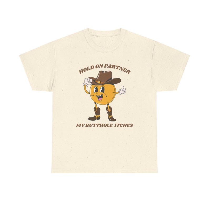 Model is wearing a gildan tee shirt in natural with a smiling cowboy giving a thumbs up and it says hold on partner my butthole itches on front in brown