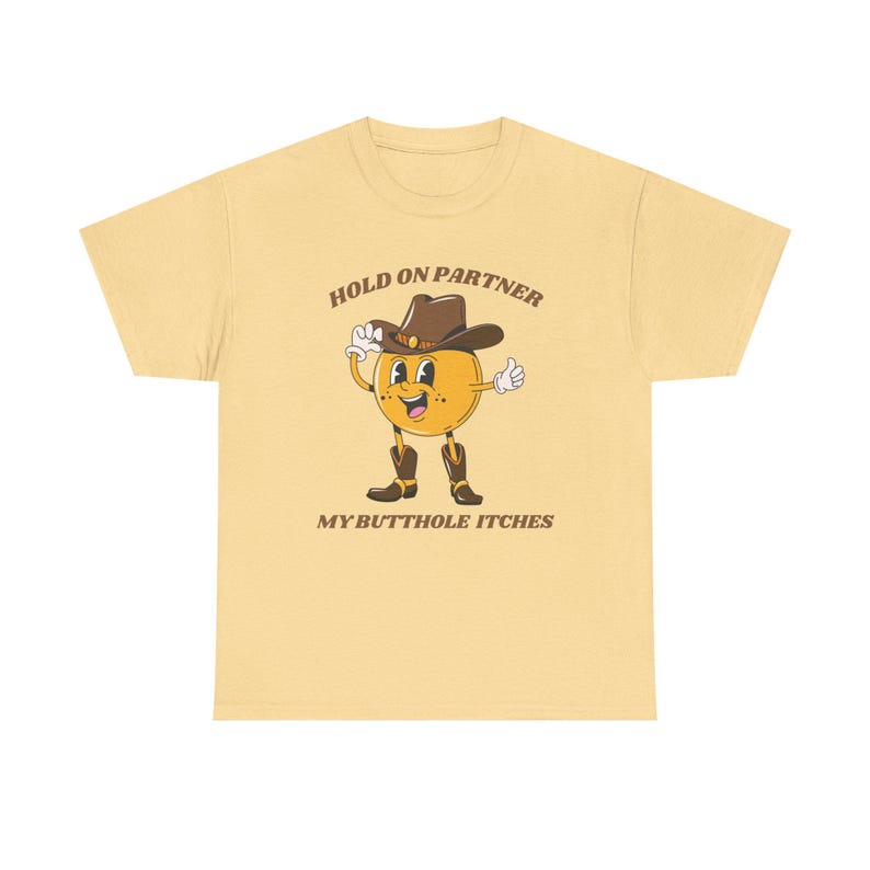 Model is wearing a gildan tee shirt in yellow haze with a smiling cowboy giving a thumbs up and it says hold on partner my butthole itches on front in brown