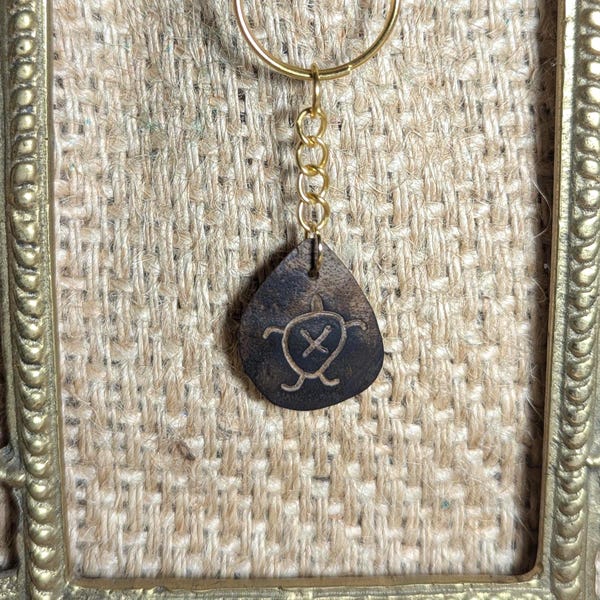May include: A gold key chain with a brown leather turtle charm. The turtle is engraved with a simple design.