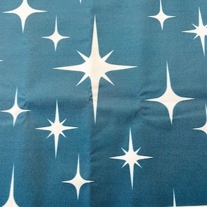 May include: Close-up of a fabric with a repeating pattern of white starbursts on a teal blue background. The starbursts vary in size and have multiple points, creating a retro, celestial design. The fabric has a slight sheen.