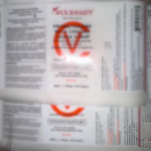 May include: A white rectangular pharmaceutical label for Wockhardt Promethazine with Codeine Cough Syrup. The label features black text on a white background with a large red letter V printed over the center. It states a net volume of 1 Pint (473 ml).