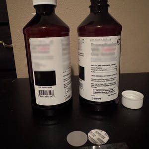 May include: Two amber plastic bottles with white screw caps, one open and one closed. The labels feature black text, barcodes, and pharmaceutical information, including dosage details for Codeine Phosphate and Promethazine Hydrochloride.