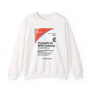 May include: A white long-sleeve sweatshirt featuring a graphic print on the chest that mimics a prescription cough syrup label. The text reads Actavis, Prometh VC With Codeine Cough Syrup, and includes ingredient details and 8FL OZ (237mL).
