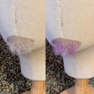 May include: A pair of small, semi-circular hair accessories attached to a mannequin head. The left accessory is a neutral, light beige color, while the right accessory features a vibrant, shimmering purple hue with fine, wispy fibers.