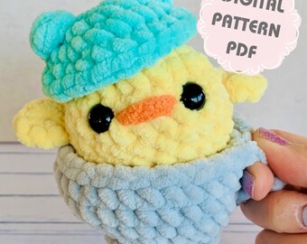 May include: A crocheted yellow chick wearing a blue crocheted hat and sitting in a blue crocheted cup. The image includes the text "DIGITAL PATTERN PDF".