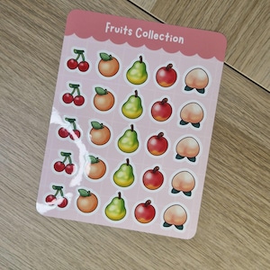 Peut inclure: Une planche d'autocollants de fruits avec une bordure rose et le texte "Fruits Collection". Les autocollants présentent des illustrations de cerises, d'oranges, de poires, de pommes et de pêches. Les autocollants sont disposés en rangées et en colonnes.