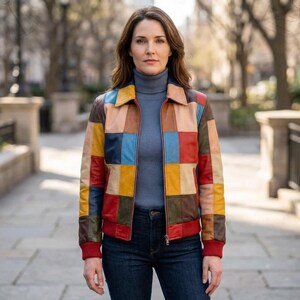 May include: A multi-colored patchwork leather jacket featuring a grid of square panels in shades of red, blue, yellow, brown, and tan. The jacket has a collared neckline, a front zipper closure, and ribbed red cuffs and hem at the waist.