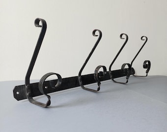 May include: A black metal wall-mounted coat rack with four decorative hooks. The hooks have a scrolled design and are attached to a horizontal bar. The rack is designed for hanging coats, hats, or other items.
