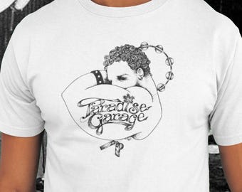 May include: White t-shirt with a black and white illustration of a person with a tambourine and the text "Paradise Garage". The background features graffiti art and a person wearing a red bucket hat.