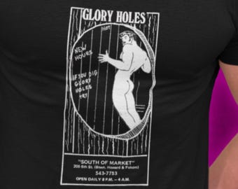 May include: A black short-sleeved t-shirt featuring a white graphic print of a figure within a circular frame. The text reads GLORY HOLES, NEW HOURS, IF YOU DIG GLORY HOLES TRY, SOUTH OF MARKET, 205 5th St, 543-7753, and OPEN DAILY 8 P.M. - 4 A.M.