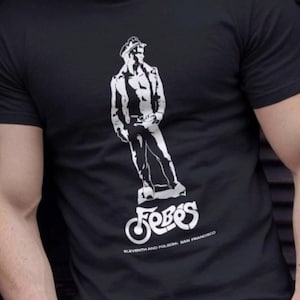May include: Black t-shirt featuring a white graphic of a man in a hat and jacket. The word "Febos" is printed below the graphic, along with "Eleventh and Polk, San Francisco". The shirt is made of a soft material.